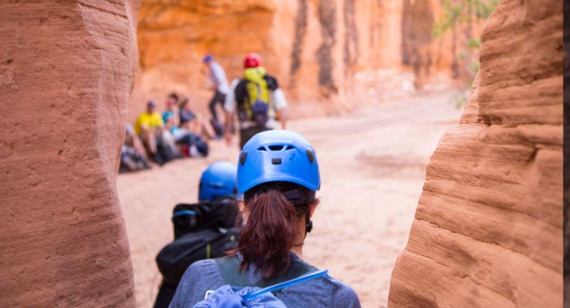 Two people exit a slot canyon toward a group of people. 